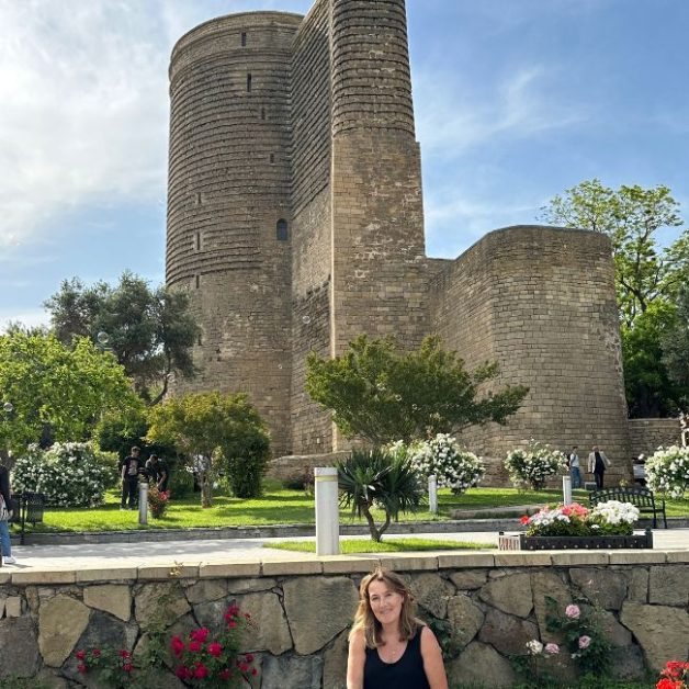 Round stone tower known as Maiden Tower Baku. Grass and flowers surround it.