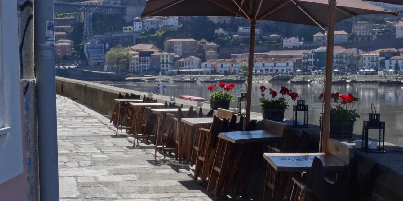 Cafe on waterfront of Porto, Portugal. Red flowers are on the Seawall and across the water red tiled roofs and white painted homes are spread out up the gentle hillside.