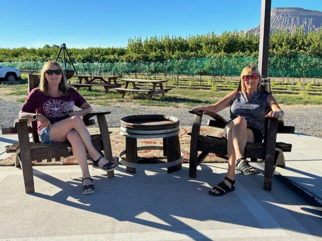 Palisade stop over on roadtrip from Denver for wine tasting. Two woman sitting in vineyard.