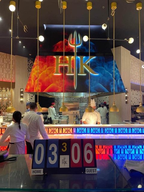 HK Restaurant in Dubai for a romantic dinner is decorated in a blue and red colour scheme. Servers are working taking food from the kitchen.
