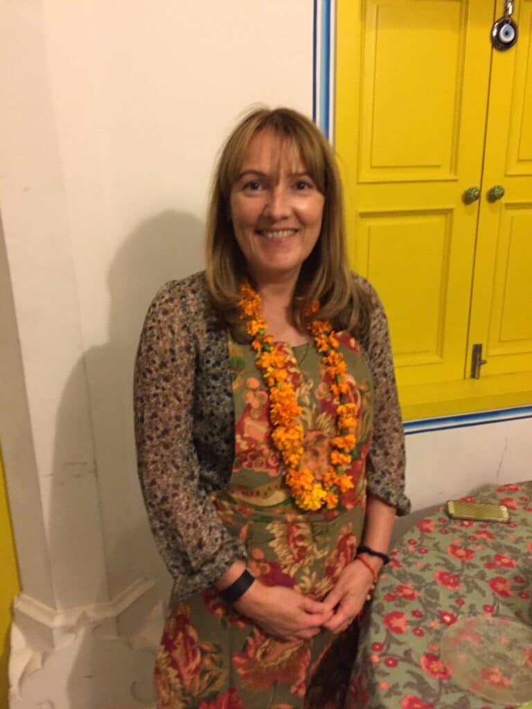 A cooking class is about to start in Jaipur at the heart of Indiaโs Golden Triangle. A woman has a flower garland around her neck and an apron on.