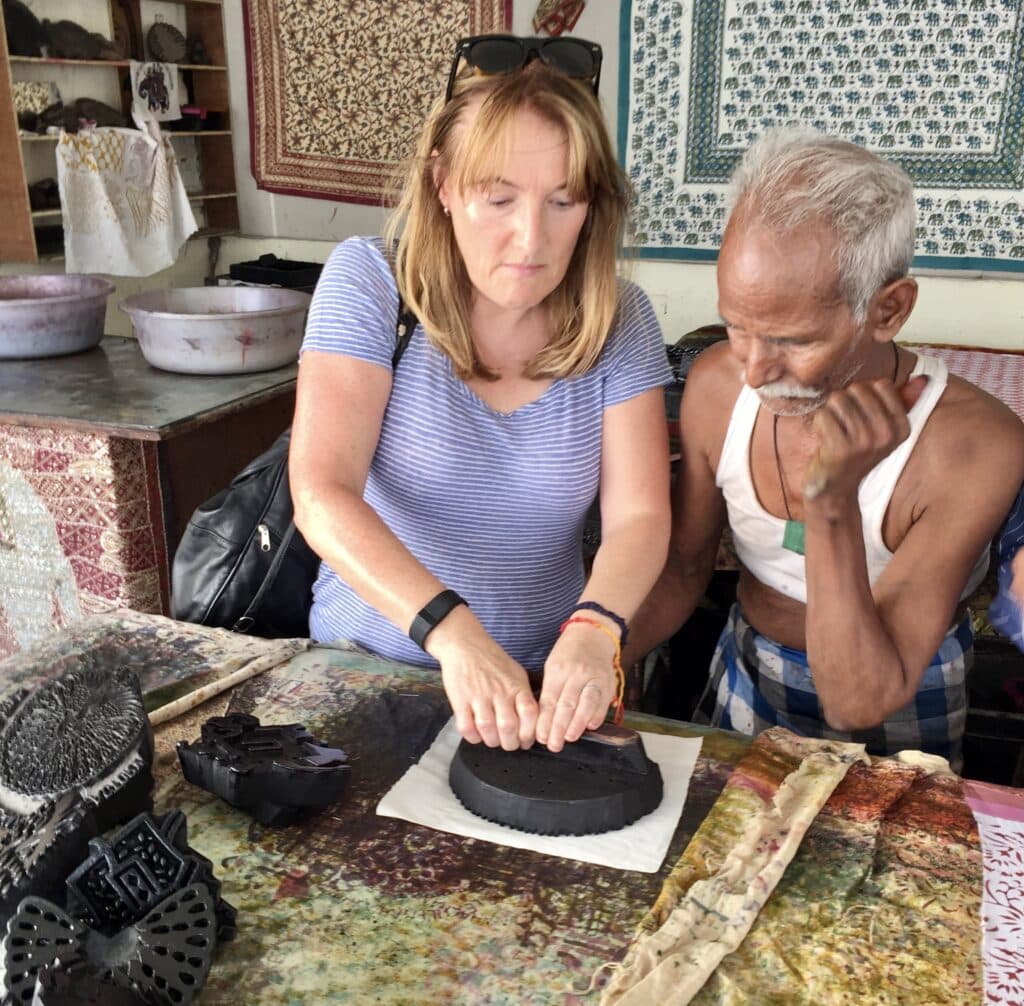 Women is using a metal hand press to print an image onto materials with the help of an artisan in Agra, Golden Triangle, India.