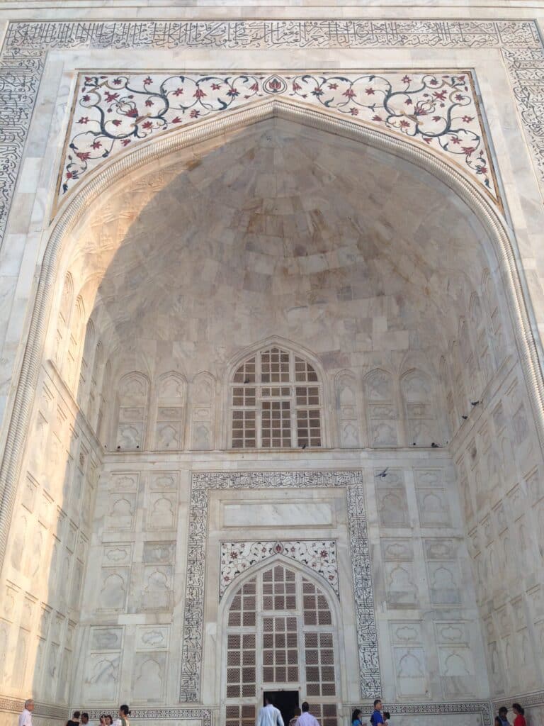 An Arch of the marble Taj Mahal building with a mosaic design in blue and red. This is in Agra on the Golden Triangle in India route.