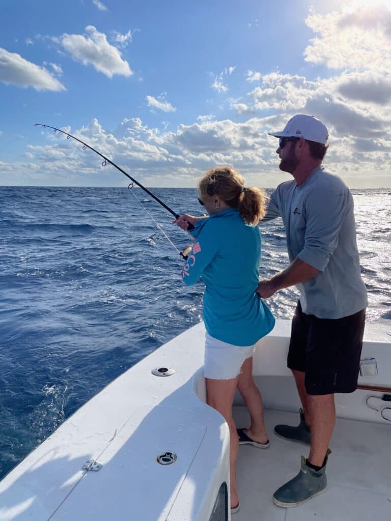 Deep Sea Fishing off Islamorada - women on boat with fishing rod and captain assisting.