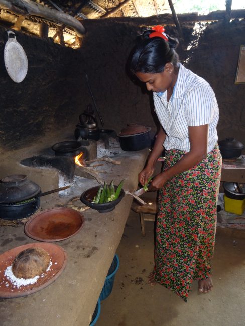 A woman is preparing Okra vegetable to cook on a wood fire. She is dressed in a long skirt that is traditional wear in Sri Lanka.