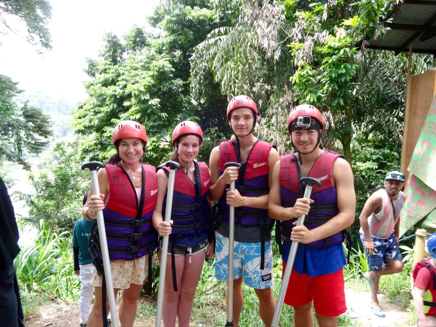 Family of tourists going river rafting. They are holding their paddles and have protective hard hats and life jackets on.