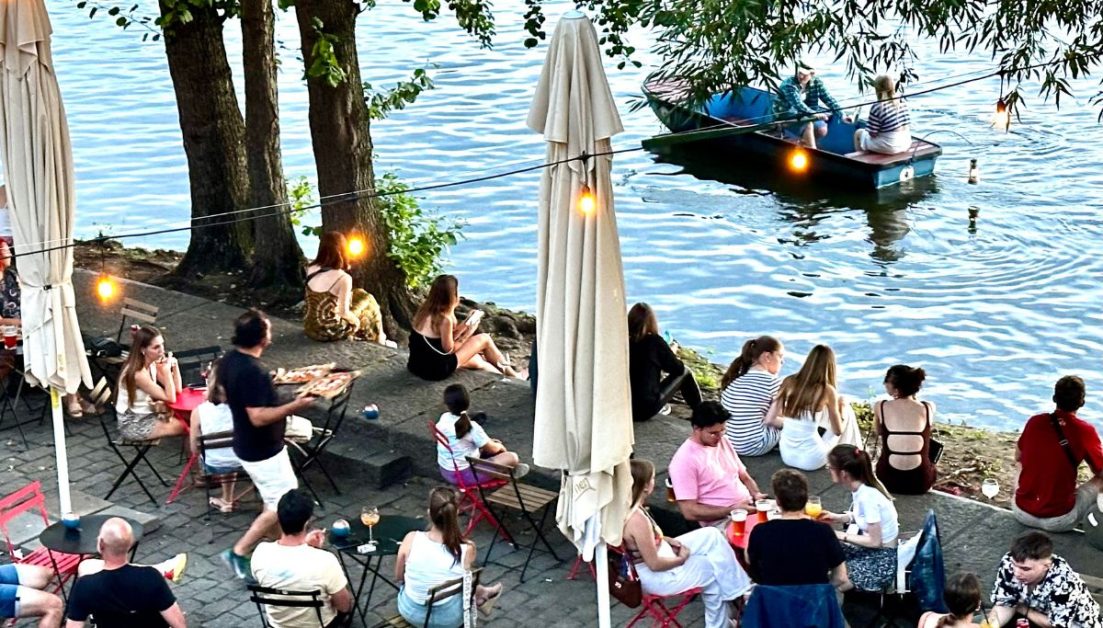 Waterside tables and chairs and people boating in the river in Prague.