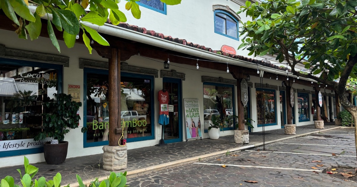 A row of souvenir shops with a shaded entrance and parking in front of the doorways.