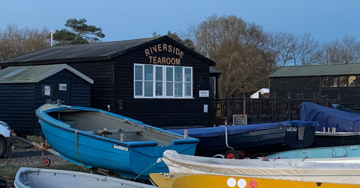 Small rowing type Boats pulled up on the quay with a building behind them saying Riverside Tearroom