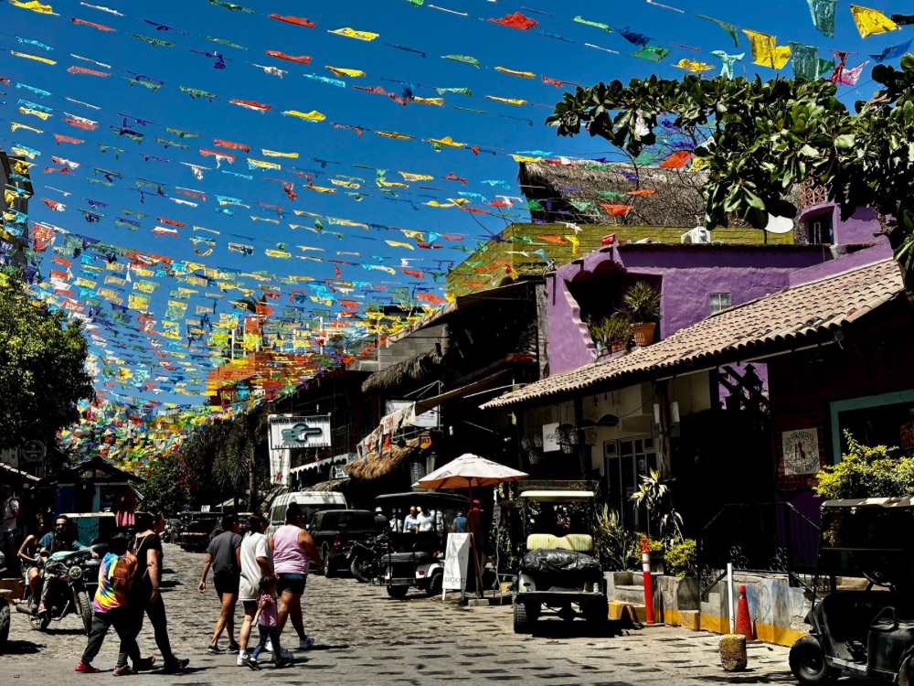 Street with bright flags overhead, golf carts and people walking around.
