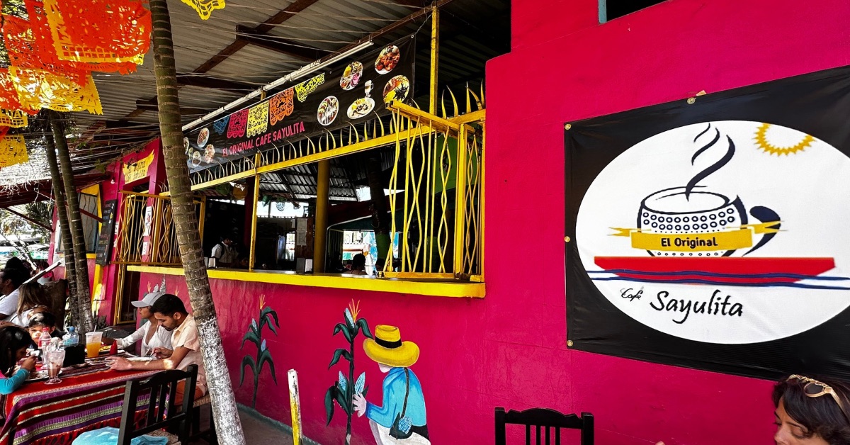 Outdoor street cafe with red walls and bright coloured flags. People sitting enjoying breakfast.
