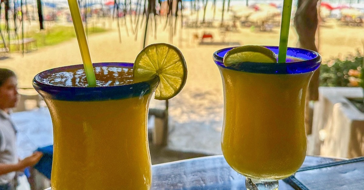 2 mango margaritas on a table at a beach front bar.