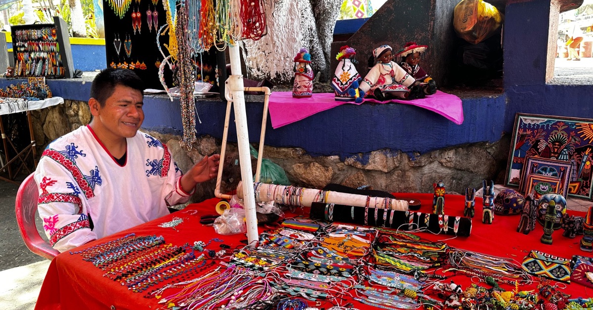 Person making bead bracelets in Sayulita sitting at a table with items for sale.