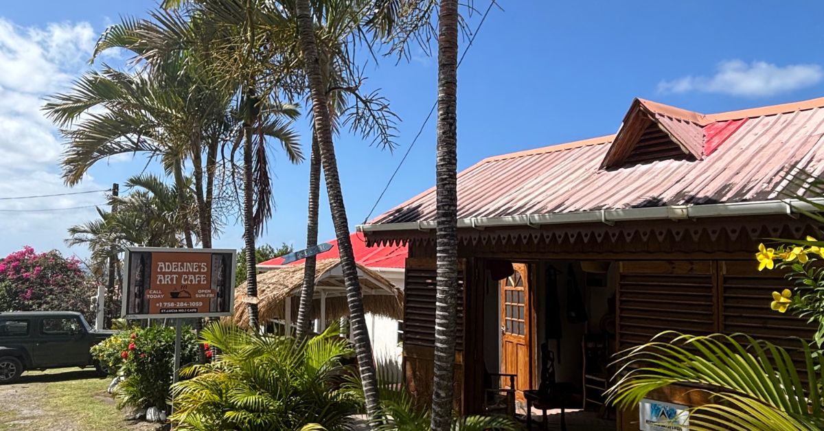 Small Brown lodge style building with palm trees outside and sign saying Adeline's Art Cafe