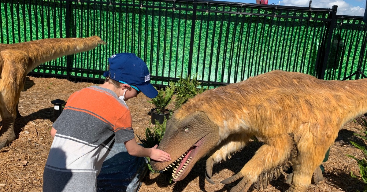Child is petting mock dinosaur at a outdoor museum.