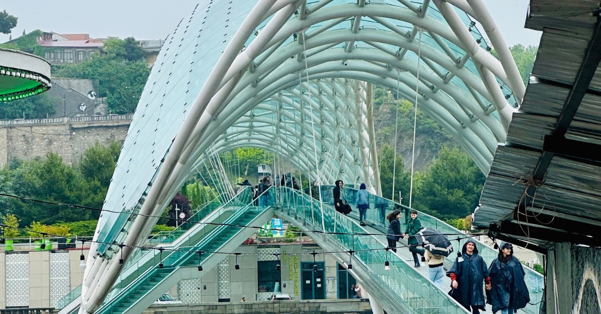 People cross a covered glass arched bridge in Tbilisi Georgia.