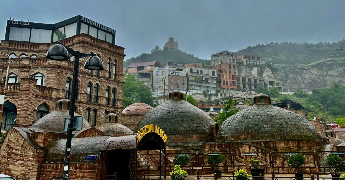 Old Town Tbilisi with stone dome sulphur springs bath houses and old multi level homes leading up a hill where there is a fortress.