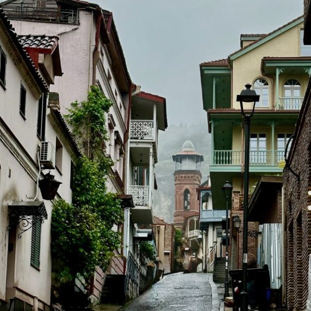 Old Tbilisi cobbled street with homes at either side of the narrow street and a church  tower at the end of the street.