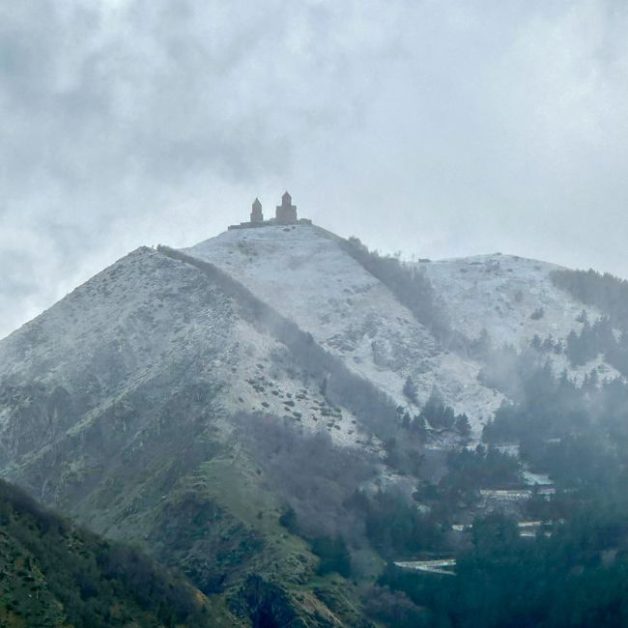 Snow-capped mountain with a small ancient church/monastery on top.